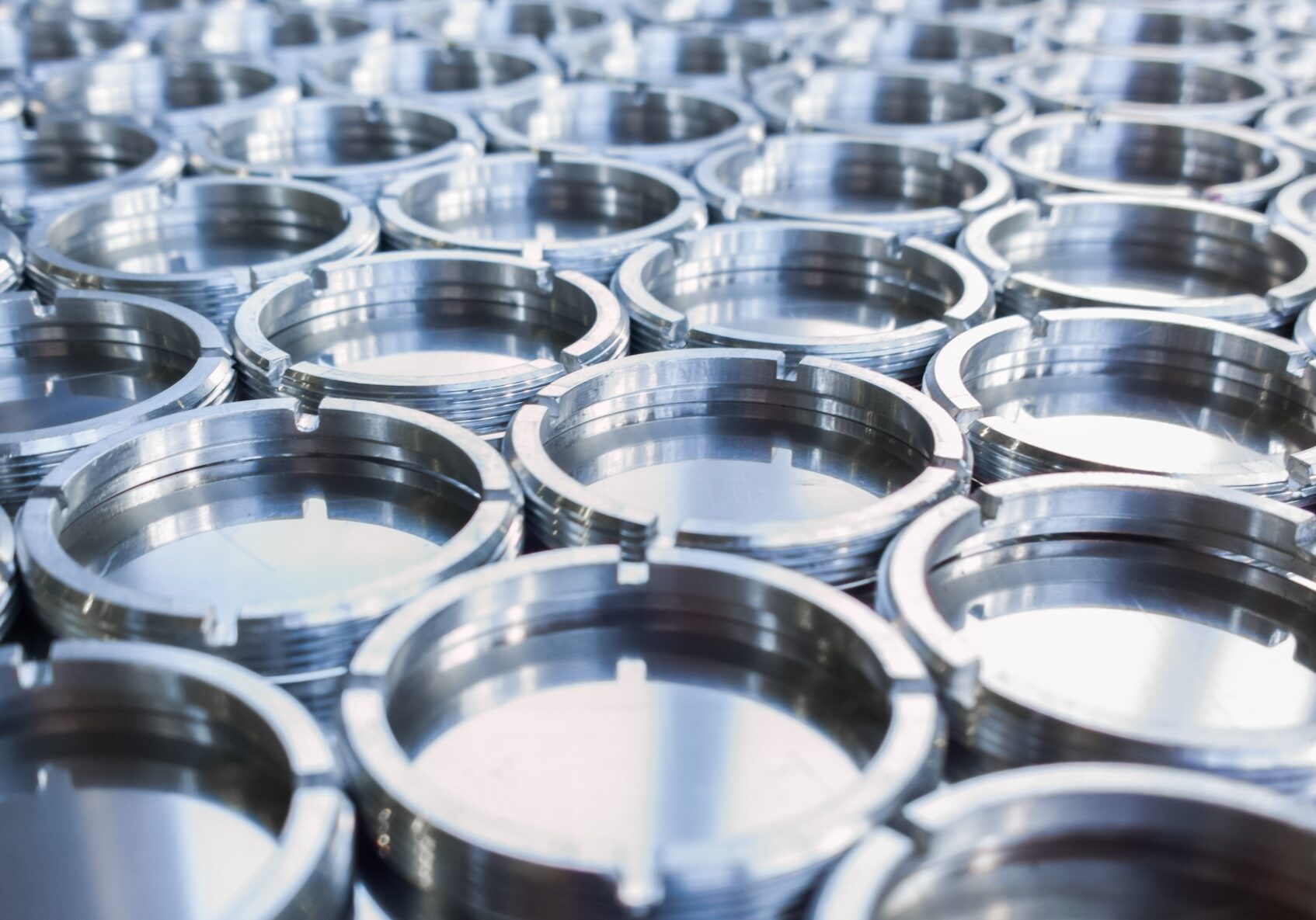 Shiny metal threaded rings after turning and milling. Silver colored rings on flat steel surface close-up full frame manufacturing background. Abstract small industrial parts batch processing concept,